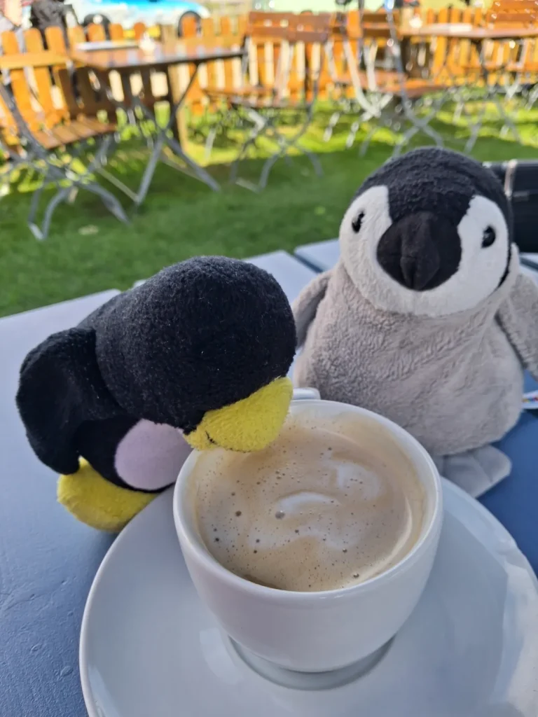 Mütux und Neville sitzen an einer Tasse mit Capuchino, Mutüx schlürft mit seinem Schnabel
