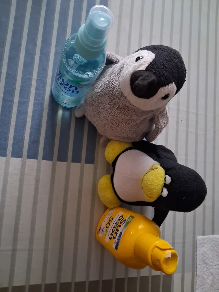 Mütux und Neville mit Sonnencreme und Aftersun an je ihrer Seite als Erinnerung.