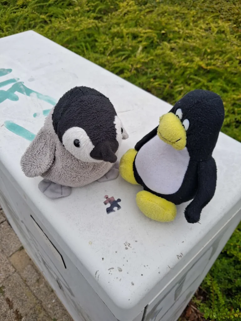 Mütux und Neville sitzen auf einem Verteilerkasten und schauen sich ihr gefundenes Puzzlestück an.