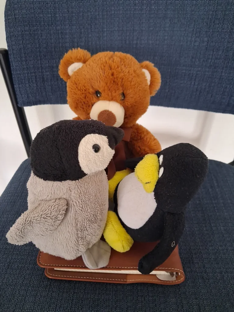 Neville und Mütux sitzen auf einen lederbraunen Kalenderplaner zusammen mit einem kleinen Plüschbraunbren auf einem blauben Stuhl.